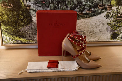 Preloved Valentino Garavani nude Rockstud Pumps with red studded straps infront of red Valentino box and behind dustbag