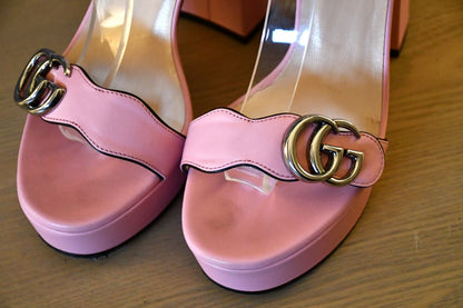 Pink platform shoes with gold Gucci logo on a wooden surface