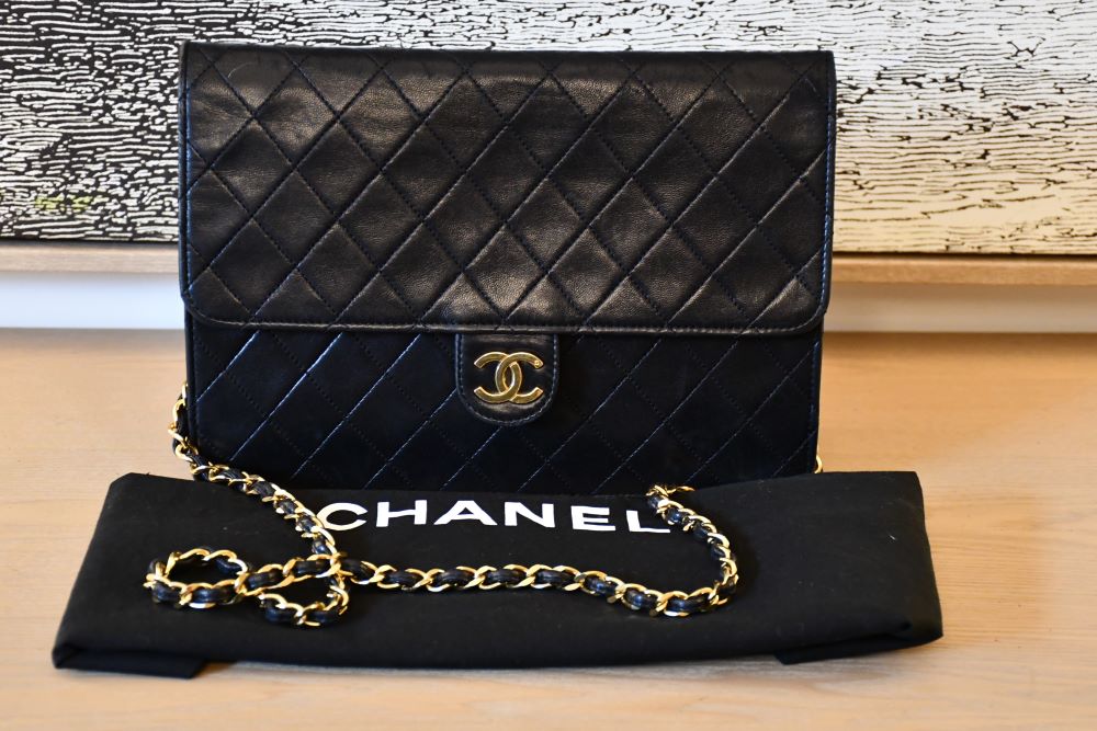 Black quilted Chanel handbag with gold chain on a black branded dustbag
