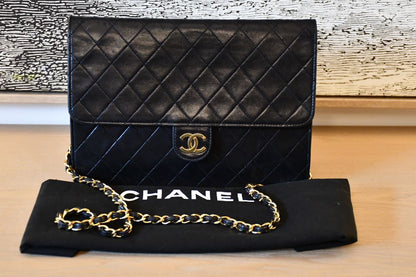 Black quilted Chanel handbag with gold chain on a black branded dustbag
