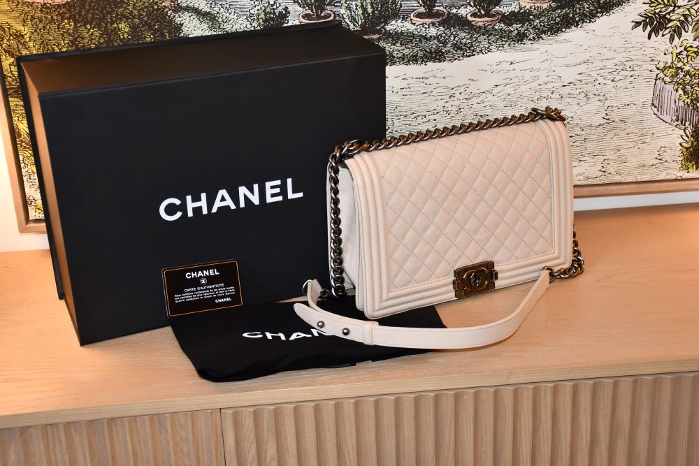 Pre owned Chanel Boy Caviar Leather Medium Bag infront of black Chanel box and on dustbag alongside authenticiy card