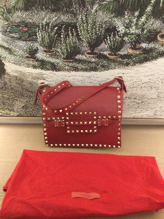 pre owned Valentino Red Leather Rockstud Buckled Bag behind dustbag