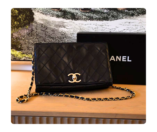 Black quilted Chanel Classic Flap medium handbag with gold chain infront of Chanel box
